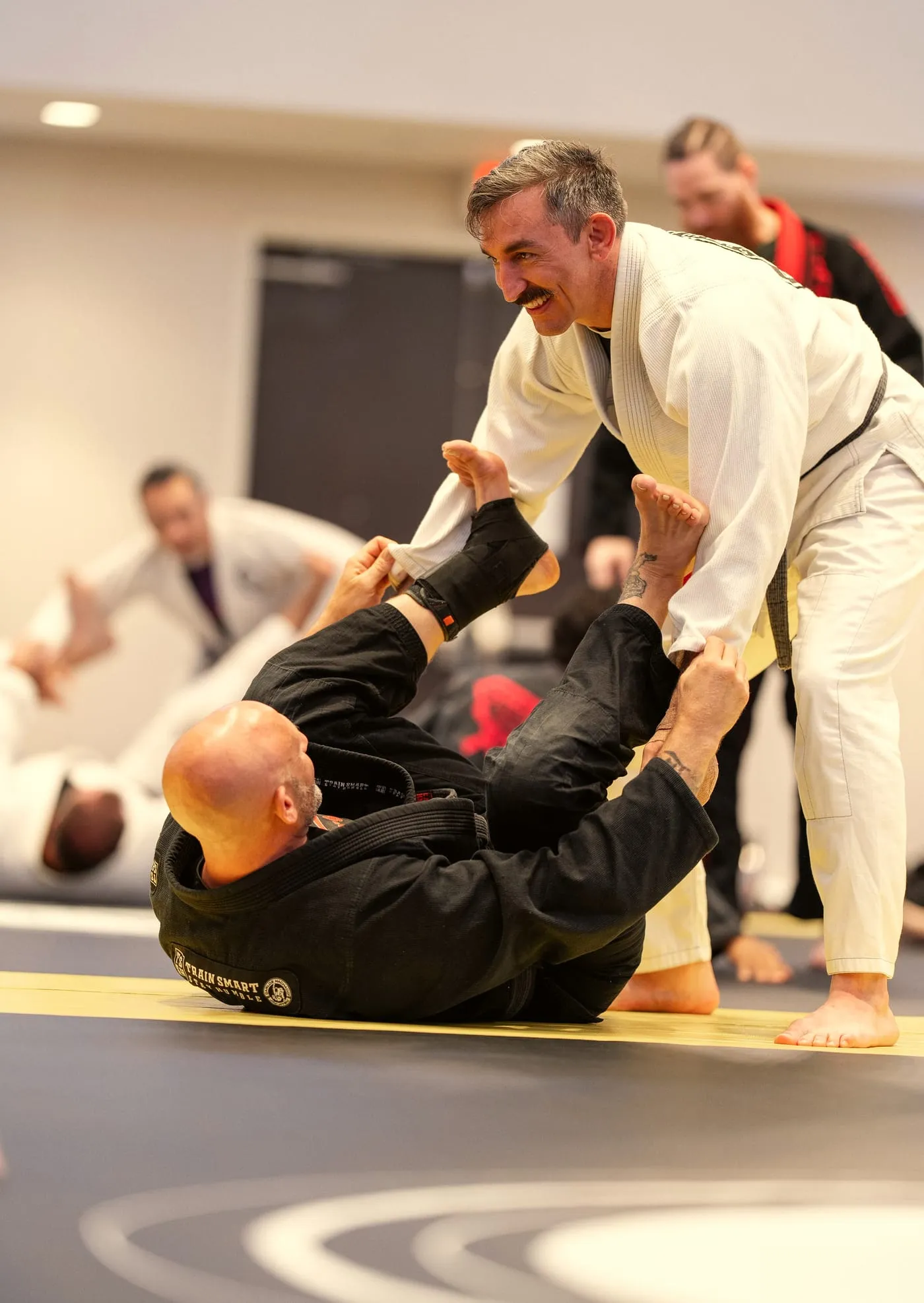 A black belt in a white gi steps into the guard of a partner in a black gi during drilling